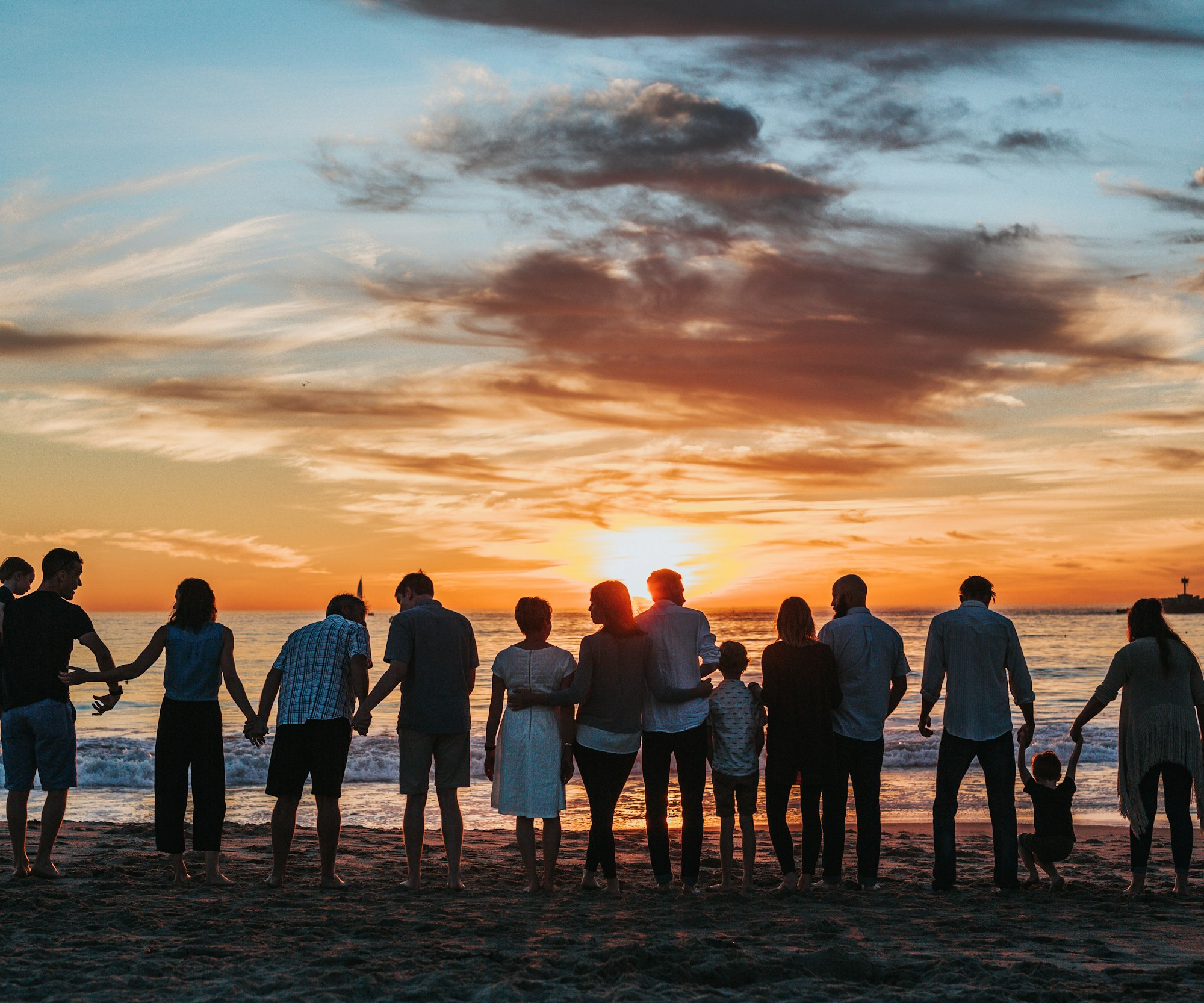 Three generations of a family holding hands on the beach at golden hour